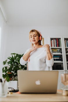 A woman using headphones for a video call at home, working remotely with a laptop.