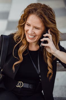 Happy businesswoman using her phone while sitting outdoors, showcasing professional style and joy.