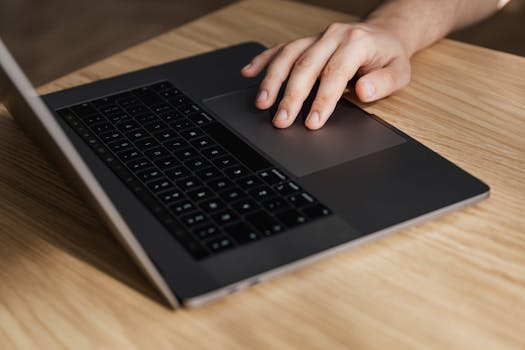 High angle of crop faceless businessman using touchpad while surfing internet on laptop at wooden table at workplace