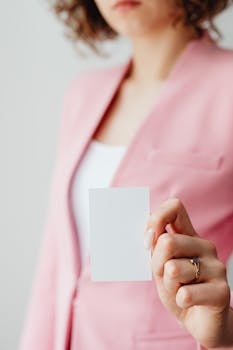 A woman in a pink blazer holds a blank card, offering copyspace for business branding.